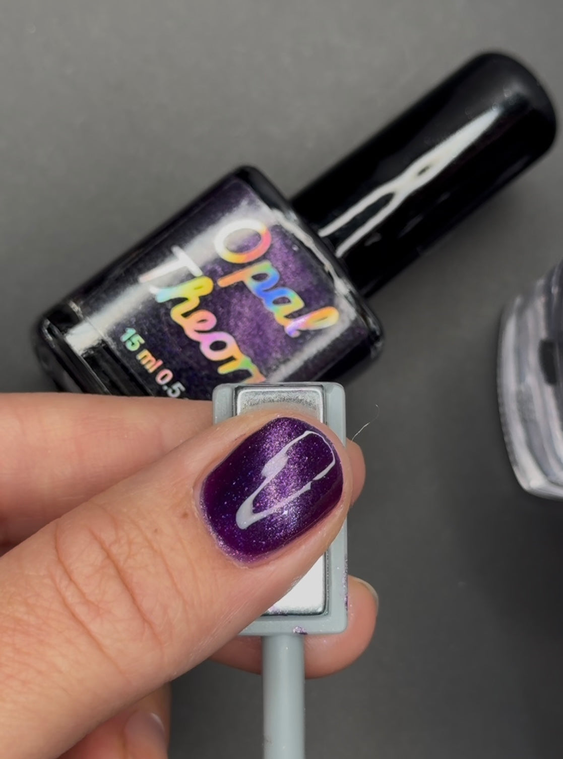 Magnetic cat eye effect shown with magnetic wand underneath a thumbnail. Opal Theory Polish.