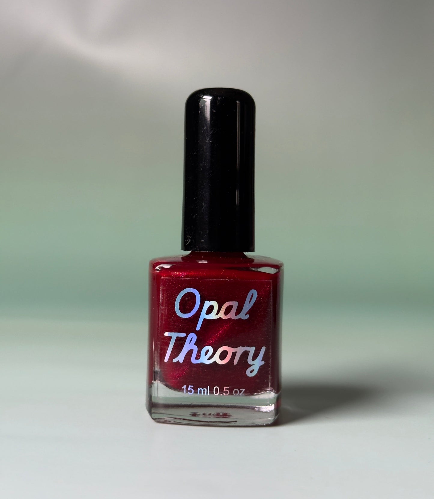 Red nail polish bottle with 'Opal Theory' label on a flat surface