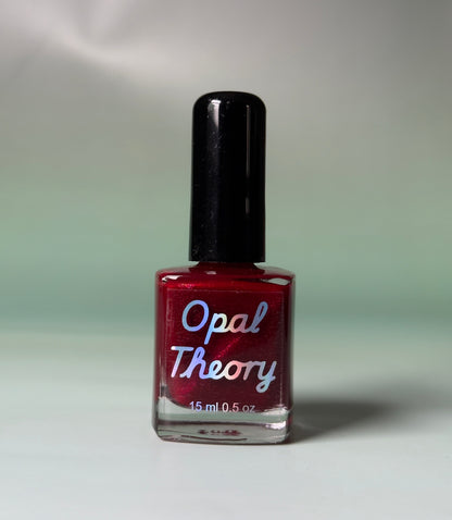 Red nail polish bottle with 'Opal Theory' label on a flat surface