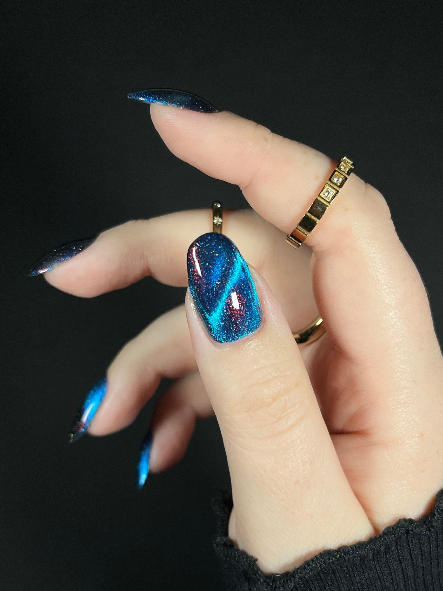 Hand with bright blue magnetic nail polish with scattered orange shimmer and scattered holo sparkles. Opal Theory Polish Cassiopeia A.