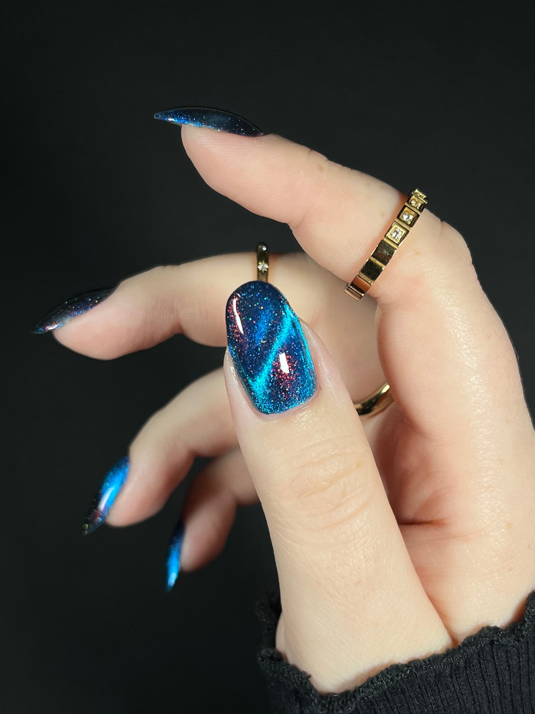 Hand with bright blue magnetic nail polish with scattered orange shimmer and scattered holo sparkles. Opal Theory Polish Cassiopeia A.