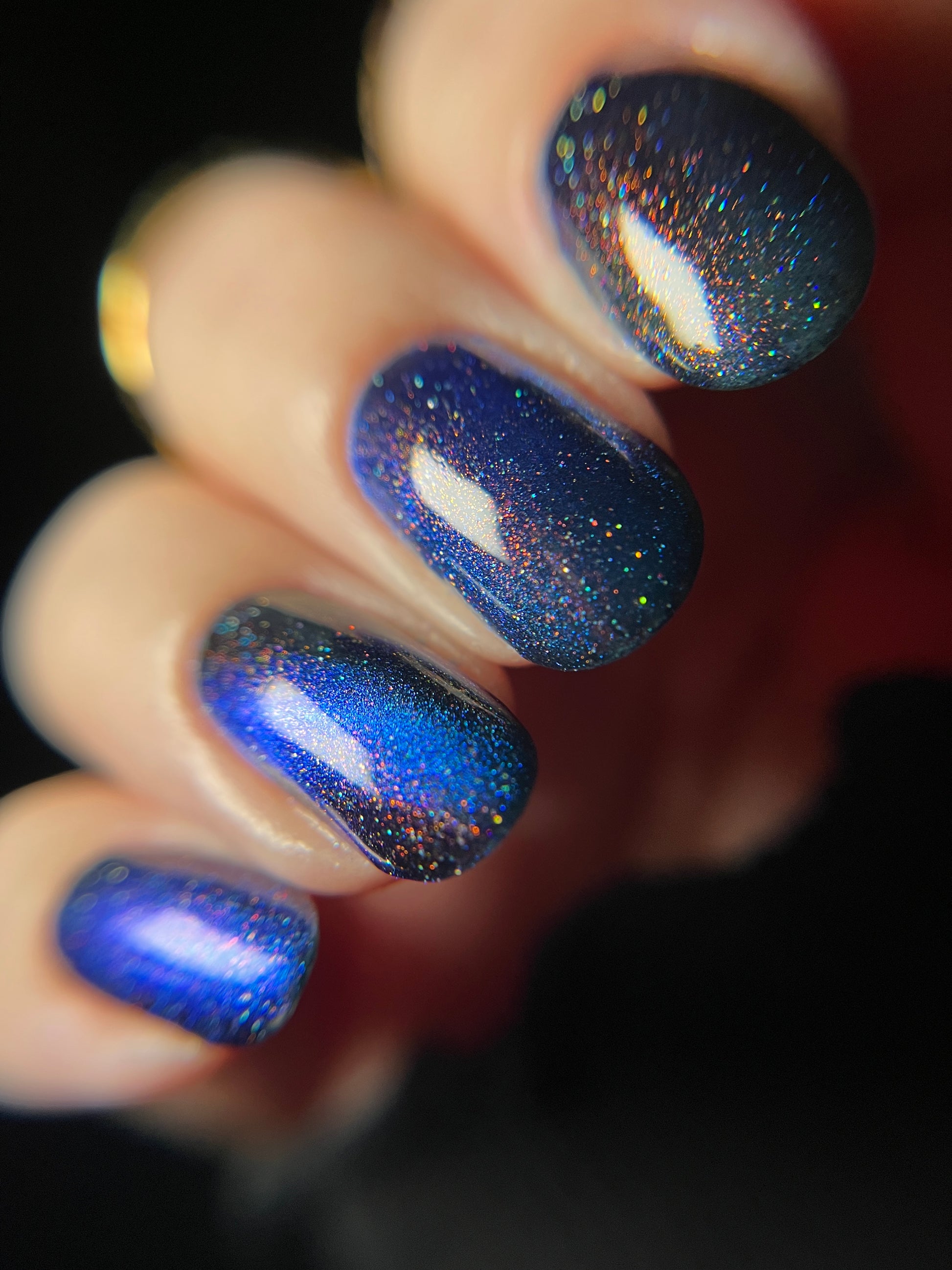 Hand with bright blue magnetic nail polish with scattered orange shimmer and scattered holo sparkles. Opal Theory Polish Cassiopeia A.