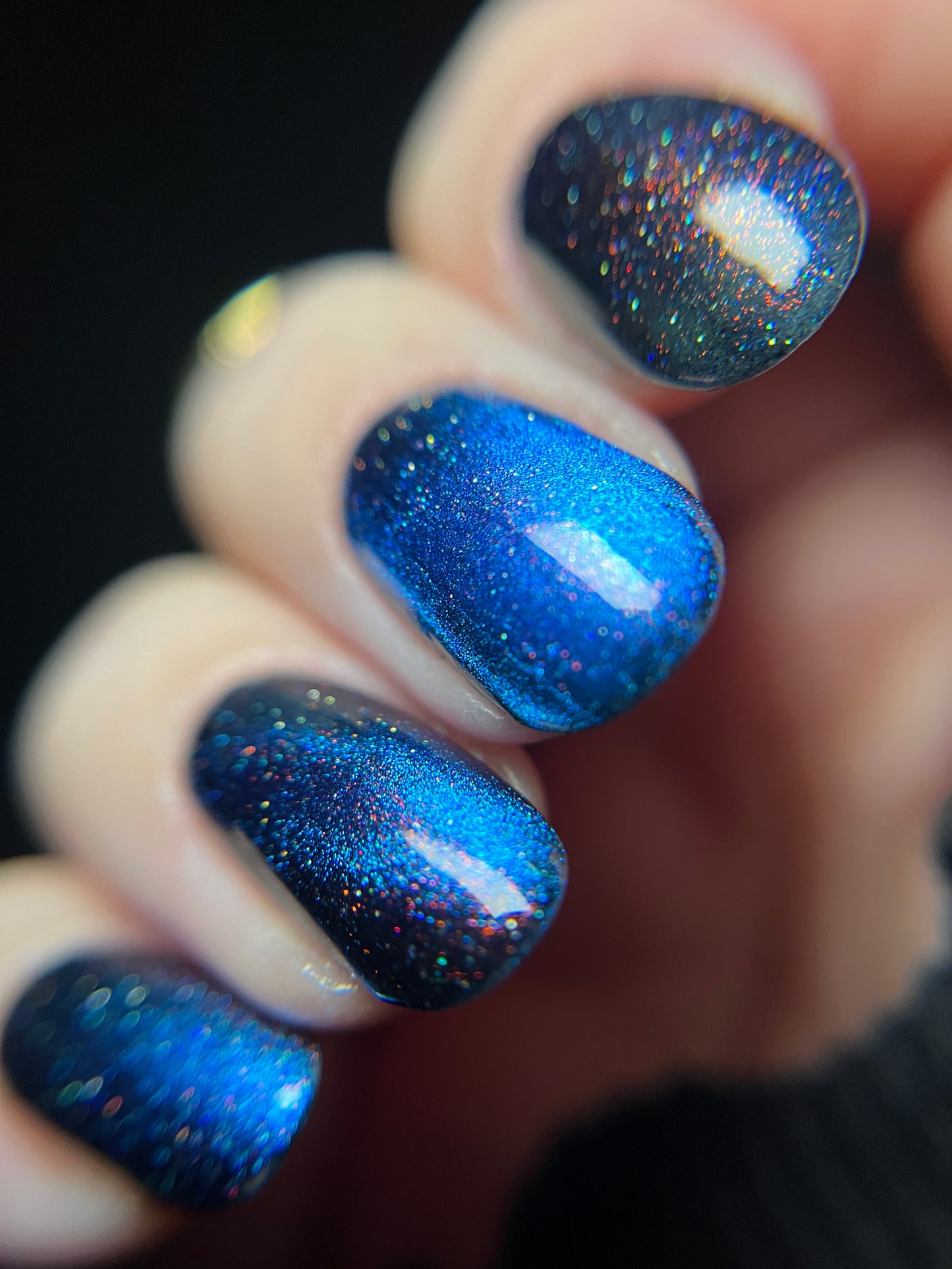 Hand with bright blue magnetic nail polish with scattered orange shimmer and scattered holo sparkles. Opal Theory Polish Cassiopeia A.