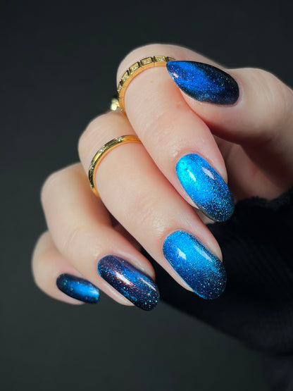 Hand with bright blue magnetic nail polish with scattered orange shimmer and scattered holo sparkles. Opal Theory Polish Cassiopeia A.