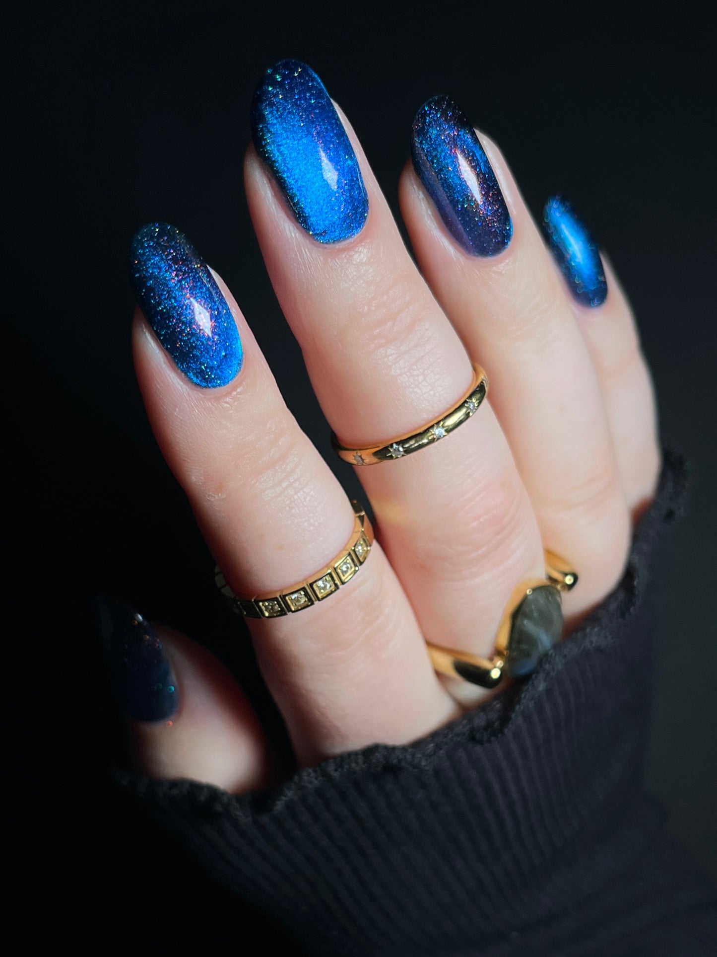 Hand with bright blue magnetic nail polish with scattered orange shimmer and scattered holo sparkles. Opal Theory Polish Cassiopeia A.