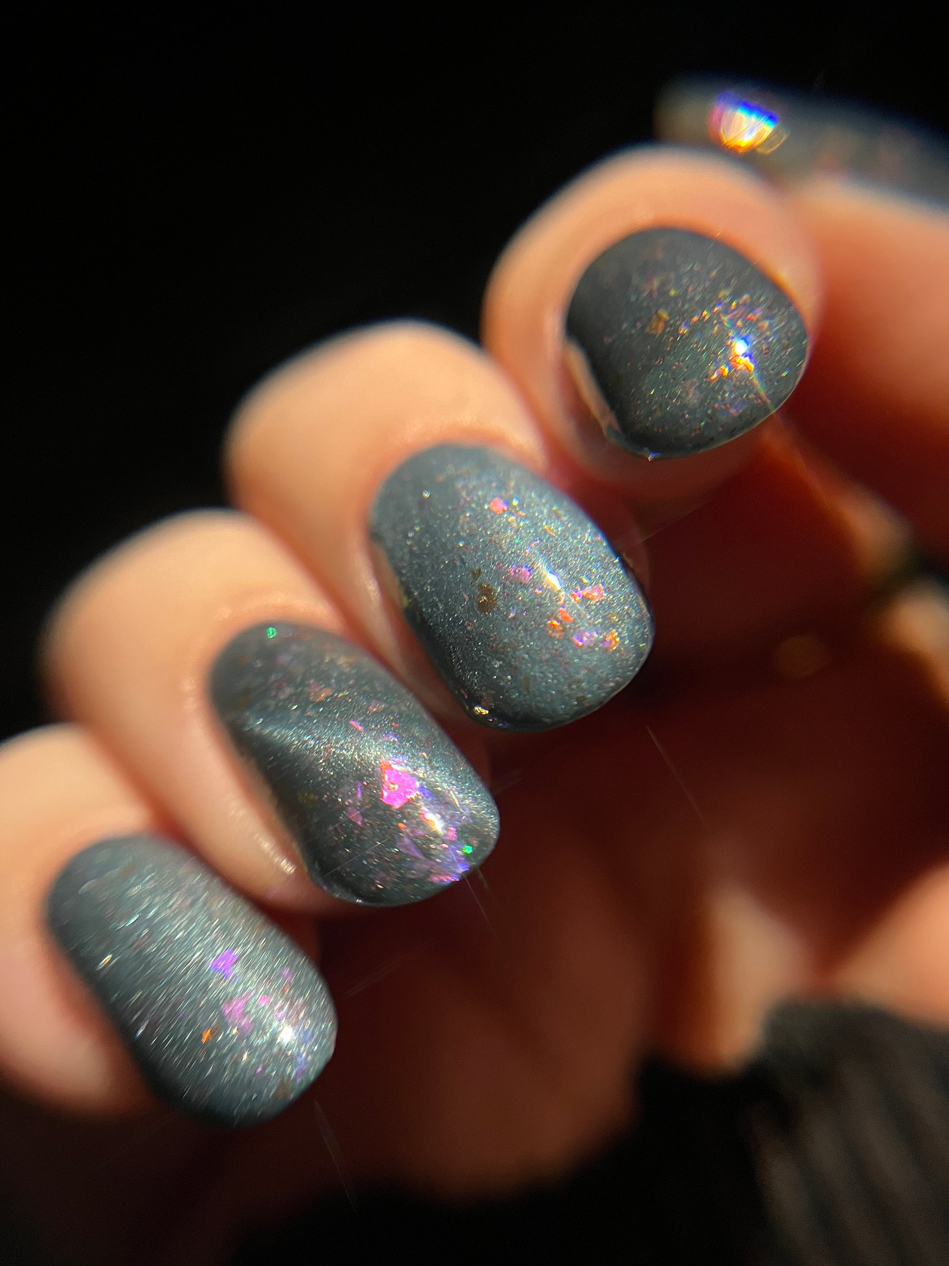 Hand with dusky gray blue magnetic nail polish with pink flakes. Opal Theory Polish Lagoon Nebula