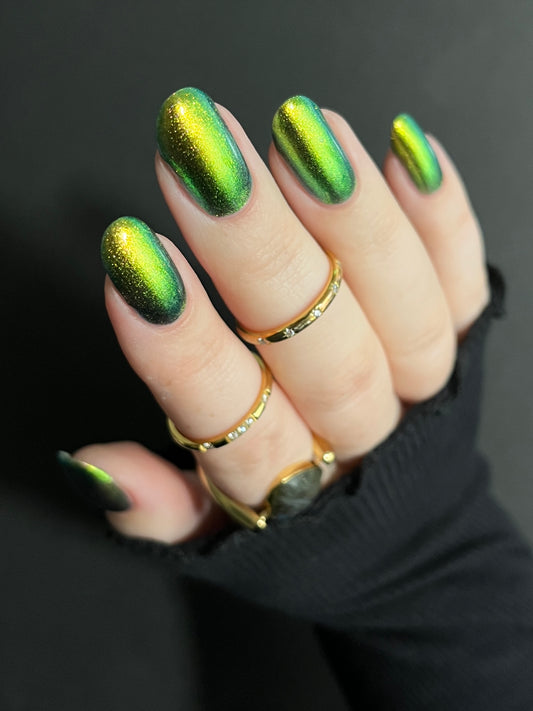 Close-up of a hand with gold-to-green multichrome metallic nail polish on a dark background Opal Theory Polish Titan, Saturn's Moon