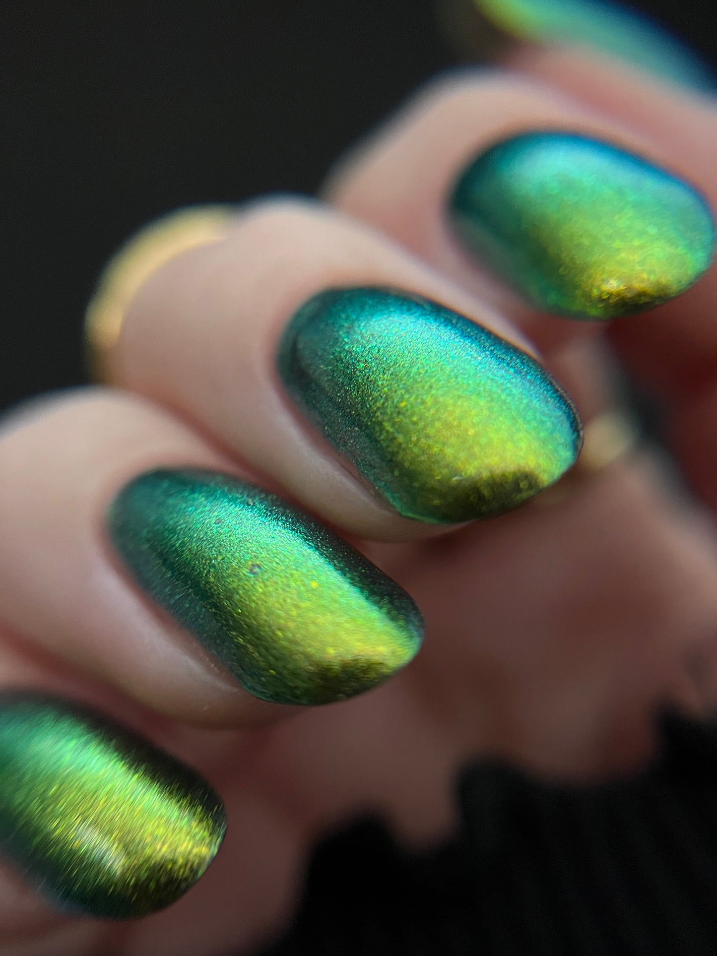 Close-up of a hand with gold-to-green multichrome metallic nail polish on a dark background Opal Theory Polish Titan, Saturn's Moon
