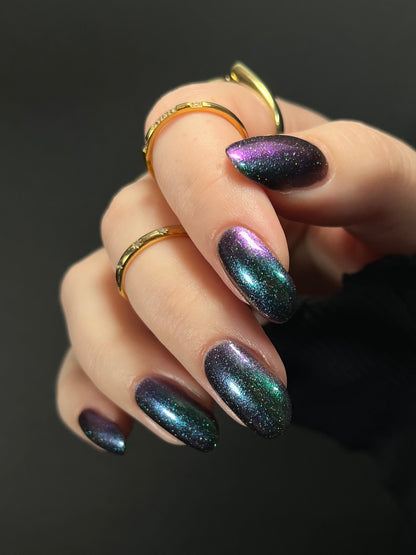 Hand with green teal to purple metallic multichrome nail polish on a dark background. Opal Theory Polish Supernova Remnant