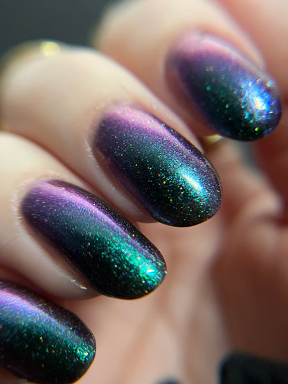 Hand with green teal to purple metallic multichrome nail polish on a dark background. Opal Theory Polish Supernova Remnant