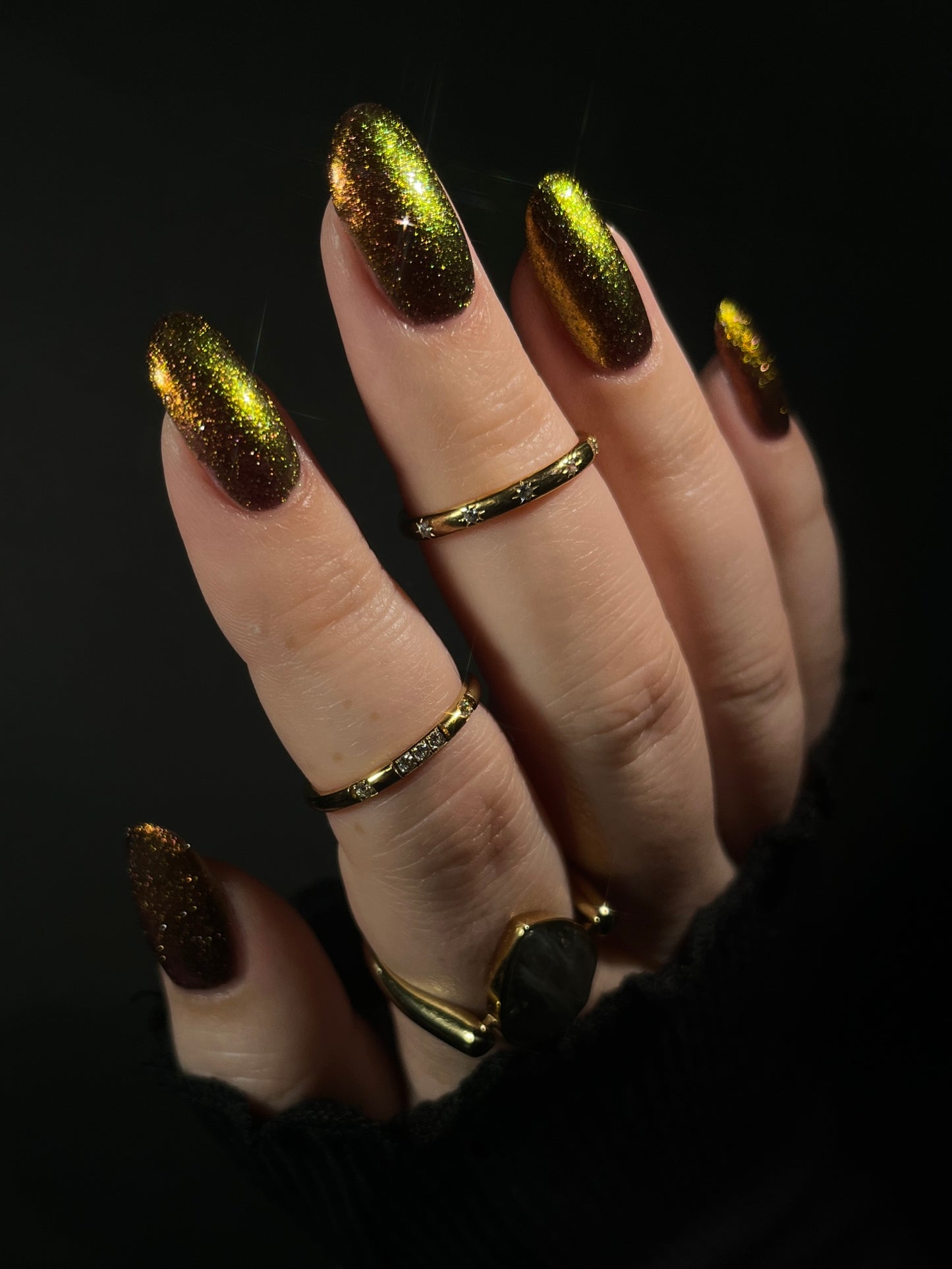 Hand with warm red gold and bronze gradient nail polish on a dark background. Opal Theory Polish Irregular Galaxy