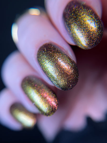 Hand with warm red gold and bronze gradient nail polish on a dark background. Opal Theory Polish Irregular Galaxy