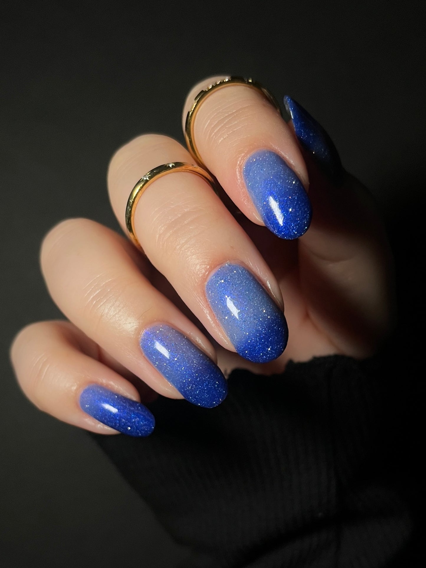 Hand with light blue to dark royal blue thermal nail polish on a dark background. Thermal nail polish with reflective glitter. Opal Theory Polish Boomerang Nebula.