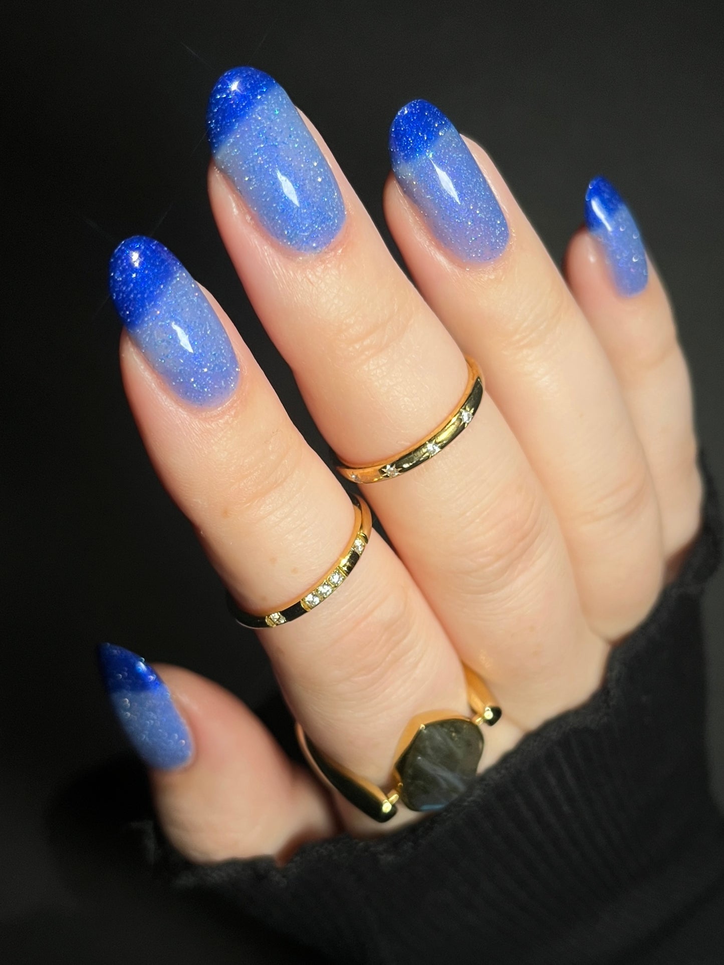Hand with light blue to dark royal blue thermal nail polish on a dark background. Thermal nail polish with reflective glitter. Opal Theory Polish Boomerang Nebula.