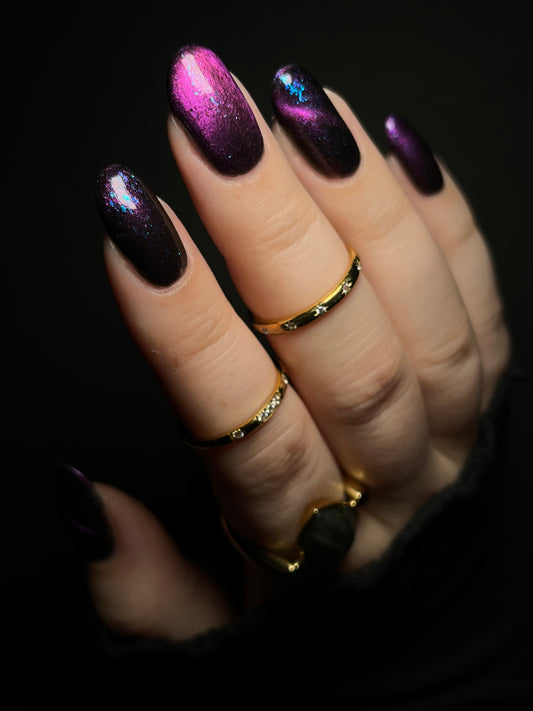 Hand with dark purple and pink magnetic nail polish with blue flakes. Opal Theory Polish Sagittarius B2