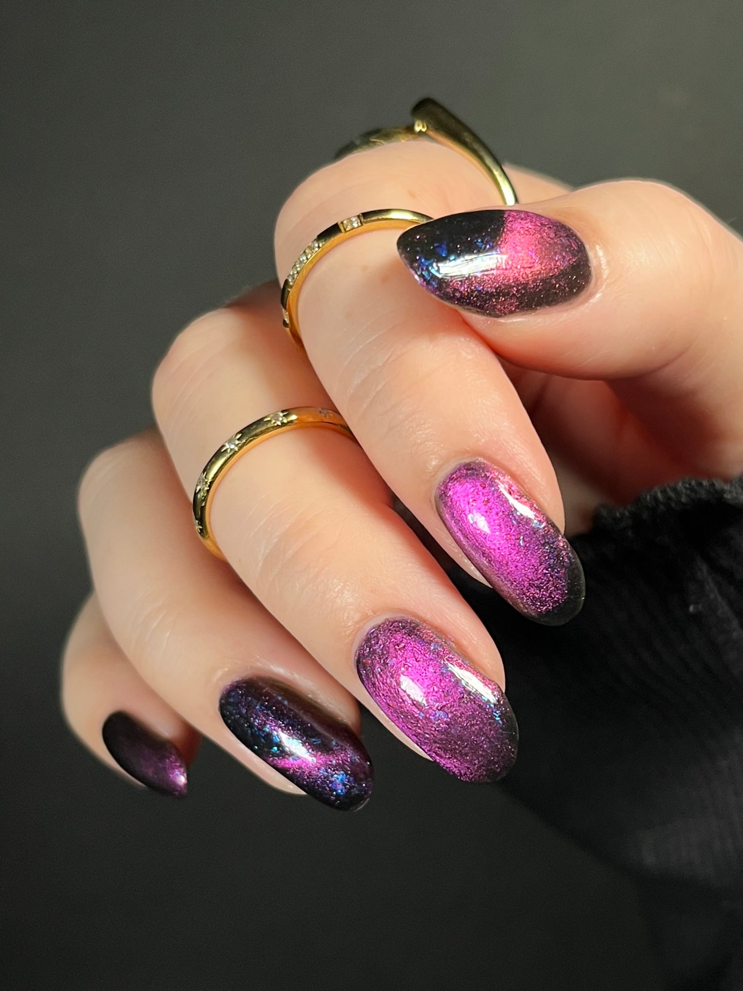 Hand with dark purple and pink magnetic nail polish with blue flakes. Opal Theory Polish Sagittarius B2