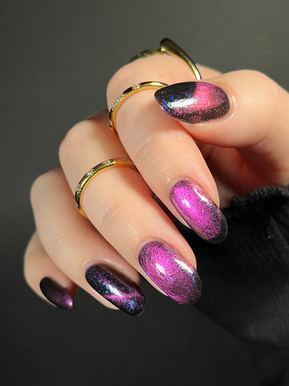 Hand with dark purple and pink magnetic nail polish with blue flakes. Opal Theory Polish Sagittarius B2