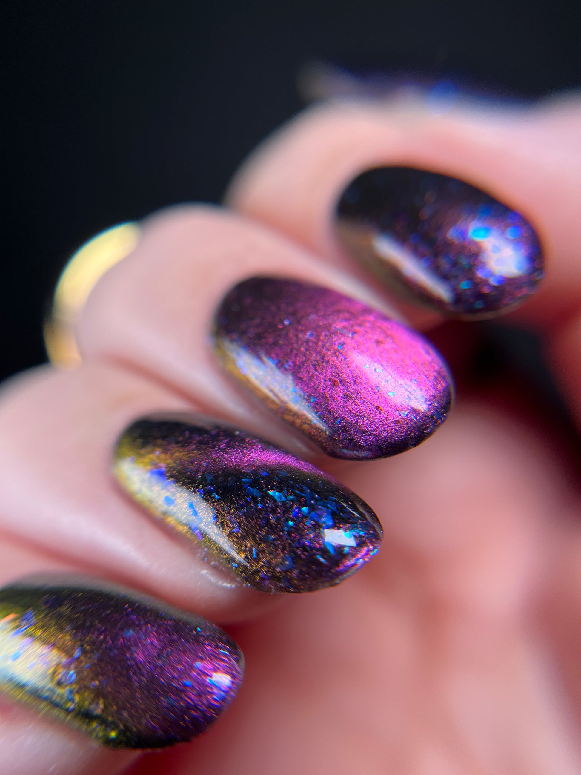 Hand with dark purple and pink magnetic nail polish with blue flakes. Opal Theory Polish Sagittarius B2