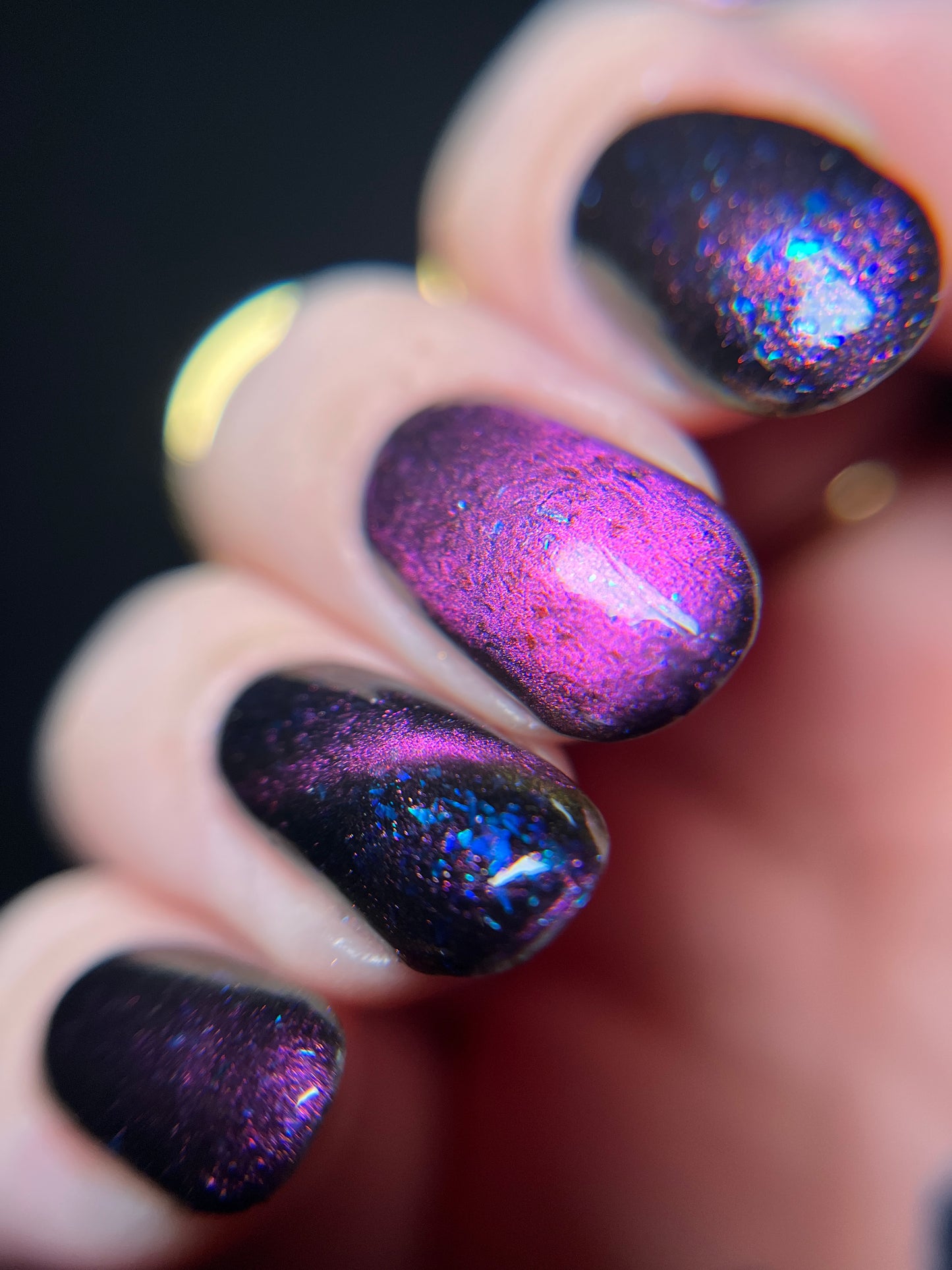 Hand with dark purple and pink magnetic nail polish with blue flakes. Opal Theory Polish Sagittarius B2