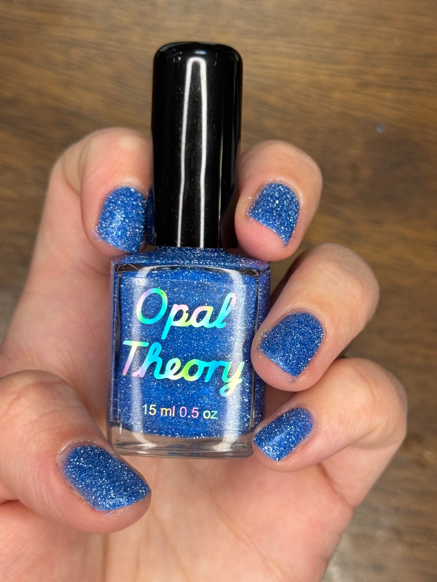 Hand holding a bottle of blue nail polish with matching nails against a wooden background
