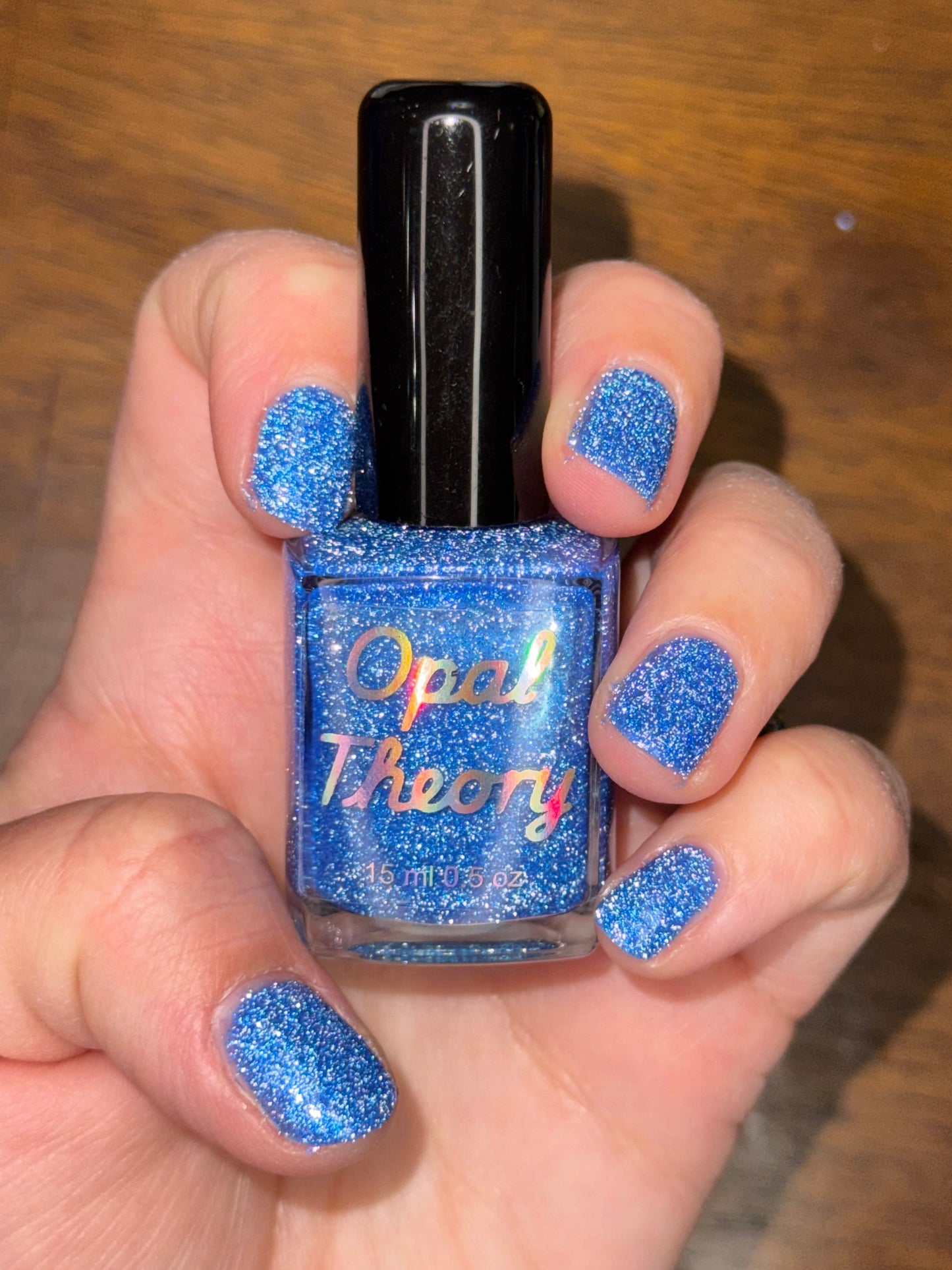 Hand holding a blue glittery nail polish bottle shown with flash.