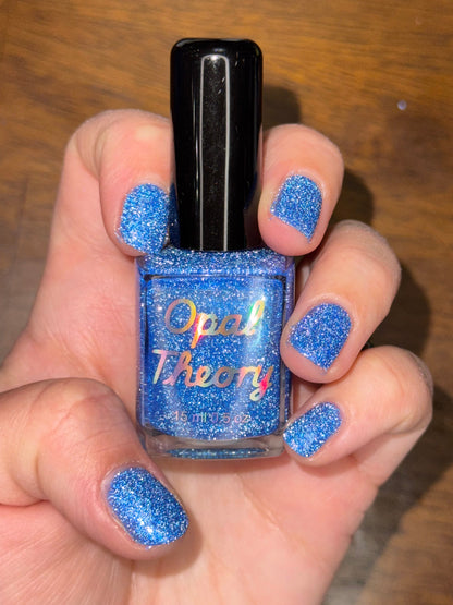 Hand holding a blue glittery nail polish bottle shown with flash.