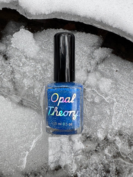 Blue nail polish bottle with 'Opal Theory' label on a snowy background with broken ice. Two if by sea, three if by ICE. ALCU charity nail polish.