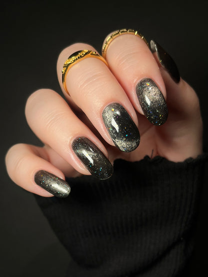 A hand with black jelly nail polish with silver magnetic pigment and silver and black holo glitter. Opal Theory Polish Deep Field