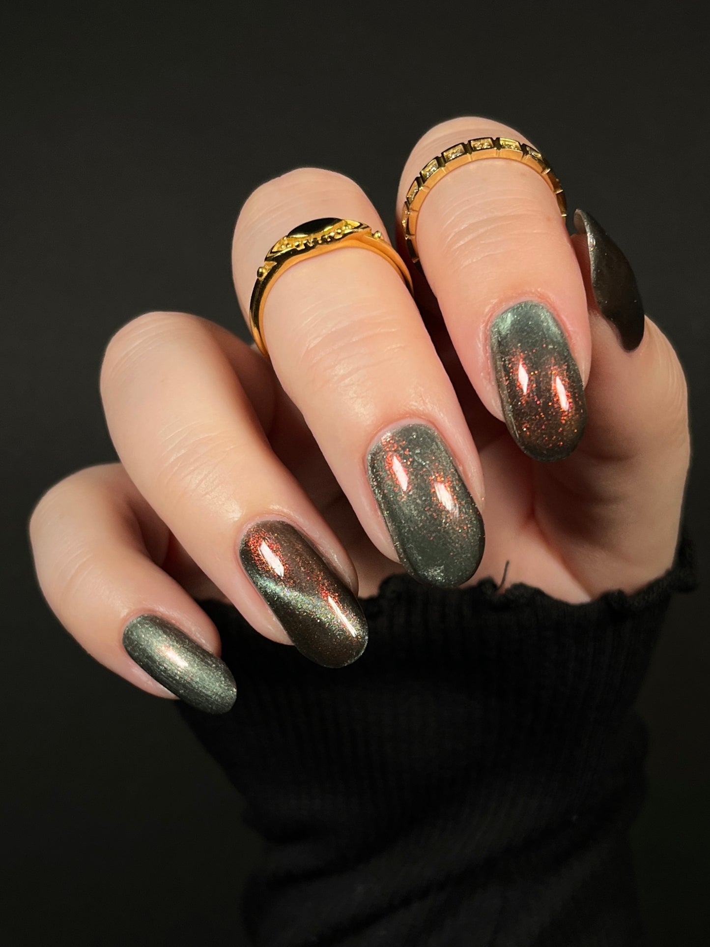 Hand with ghostly gray magnetic nail polish with orange to red shifting shimmer on a dark background. Opal Theory Polish The Pillars of Creation.