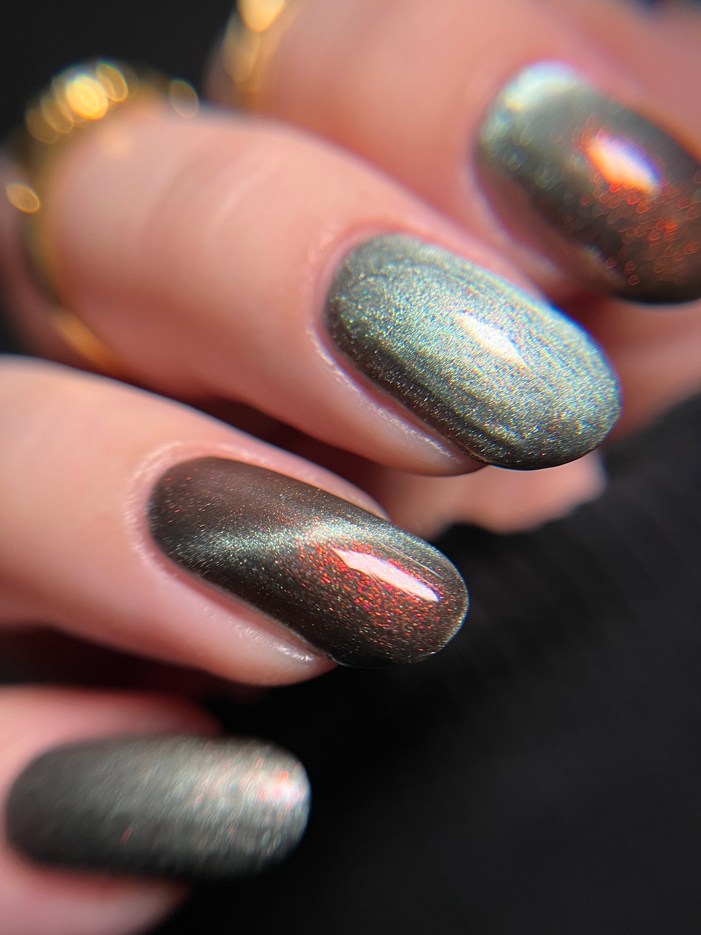 Hand with ghostly gray magnetic nail polish with orange to red shifting shimmer on a dark background. Opal Theory Polish The Pillars of Creation.