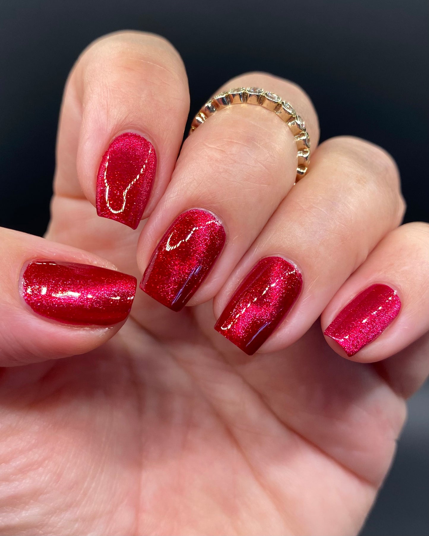 Hand with red glittery nail polish on a dark background